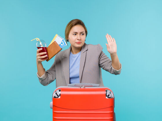 成人前景度假中的女性拿着果汁和浅蓝色背景的机票旅行度假海上飞机航行拒绝微笑