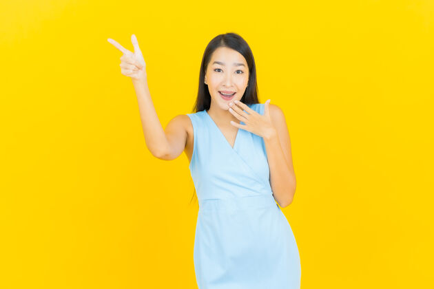 卷发在黄色墙壁上描绘美丽的亚洲年轻女子微笑的动作学生女性Swoosh