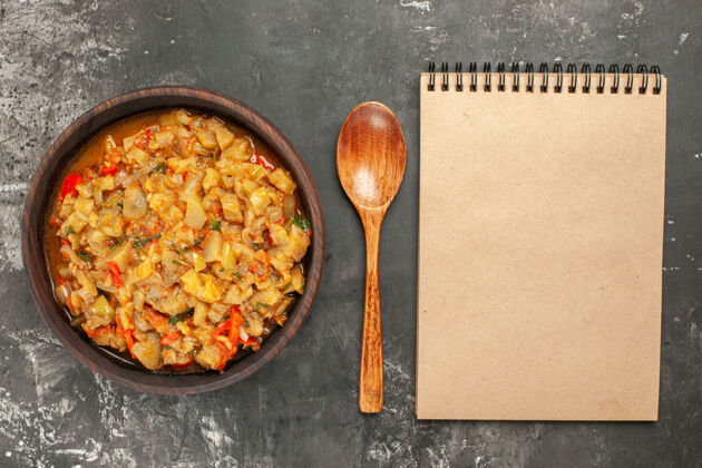 深色顶视图烤茄子沙拉在碗勺笔记本上黑暗的表面农产品午餐餐具