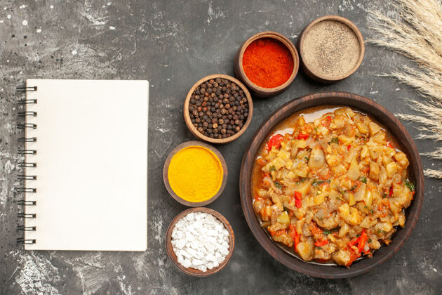 一餐顶视图烤茄子沙拉在碗和不同的香料在小碗一个笔记本在黑暗的表面小香料烤