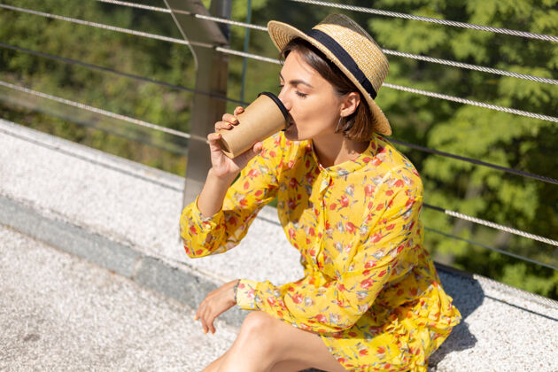 旅游穿着黄色夏装 戴着帽子 喝着咖啡 享受阳光的女人的户外肖像放松桥梁旅游者