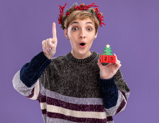 圣诞树令人印象深刻的年轻漂亮女孩戴着圣诞花环手持圣诞树玩具和日期看着相机指向上孤立的紫色背景玩具圣诞快乐印象