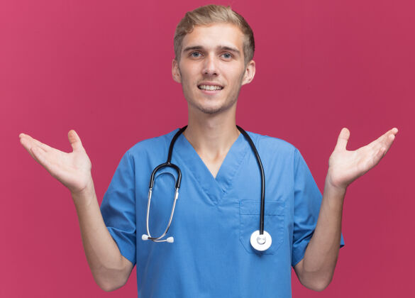 公民微笑着的年轻男医生穿着医生制服 听诊器摊开双手隔离在粉红色的墙上衣服人穿着