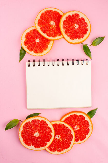 柑橘美味的葡萄柚与粉红色表面上的记事本俯视图水果新鲜醇香