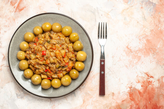 李子烤茄子沙拉和腌李子在裸体表面的叉子上的顶视图水果裸体盘子