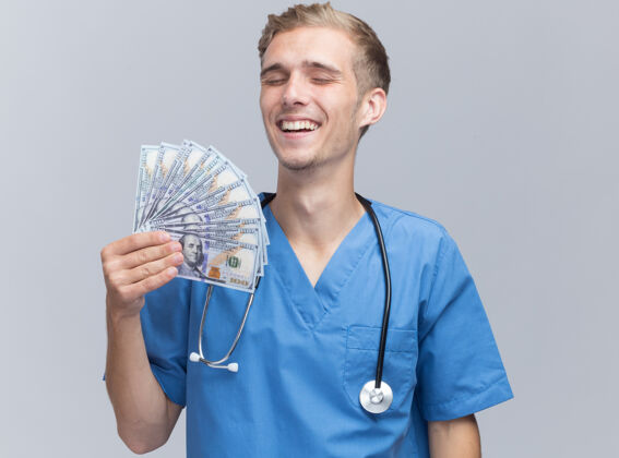 人微笑着闭上眼睛年轻的男医生穿着医生制服听诊器拿着现金隔离在白墙上站着穿着听诊器