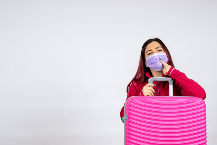 旅游正面图：戴着无菌口罩的粉红色袋子的年轻女性思考白色墙壁旅行彩色假期柯维德妇女病毒大流行女人快乐风景