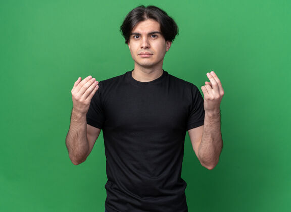 帅一个年轻帅哥 穿着黑色t恤 在绿色的墙上显示着一种孤立的姿态秀男人小费