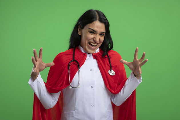 穿愤怒的年轻超级英雄女孩穿着医用长袍 听诊器摊开双手隔离在果岭上愤怒听诊器医疗