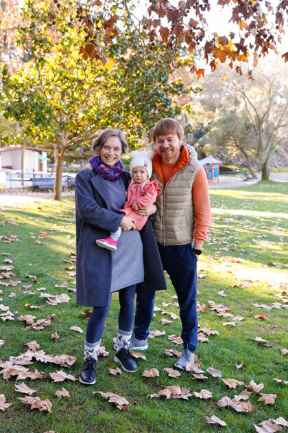 外面快乐的一家人一起站在秋天的公园里 微笑着快乐的妈妈抱着可爱的宝宝欢呼成人婴儿