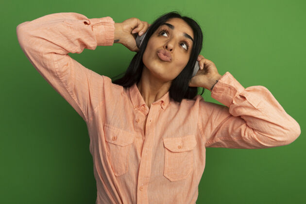 壁板高兴地看着身边年轻漂亮的女孩穿着粉红色的t恤和耳机隔离在绿色的墙上女孩耳机年轻