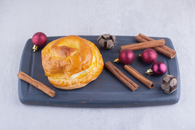 肉桂甜甜的面包 肉桂棒和圣诞装饰品放在白色表面的木盘上芳香美味烘焙