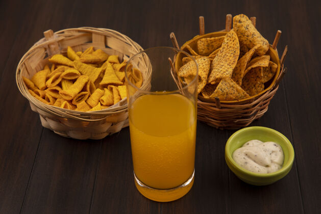 玻璃木桌上的绿色碗上放着一杯橙汁和酱汁 桶上放着玉米小吃 桶上放着辣薯条的俯视图橙色小吃顶部