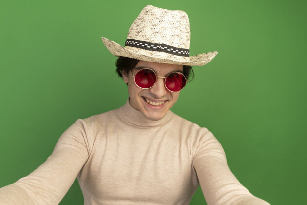 年轻人微笑的年轻帅哥戴着帽子戴着眼镜隔离在绿色的墙上帅气抱着小伙子