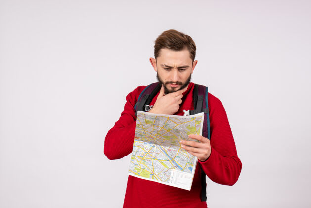 颜色正面图年轻男性游客背着背包拿着地图上的白色墙壁柯维德飞机度假情感病毒飞行色彩人成人情绪