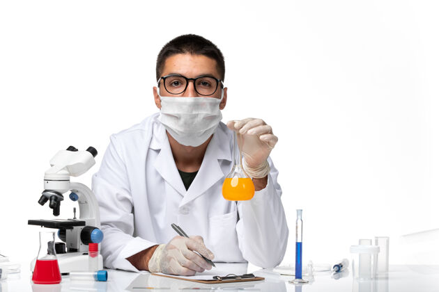 医疗正面图：男医生穿着白色医疗服 戴着口罩 在白色办公桌上拿着溶液工作大流行医院套装