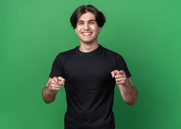 姿态微笑的年轻帅哥穿着黑色t恤 在绿色的墙上展示你的孤立姿态帅气秀男人