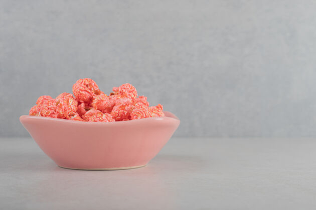 垃圾食品粉红色的碗里放着一份放在大理石背景上的爆米花糖糖果爆米花甜味剂