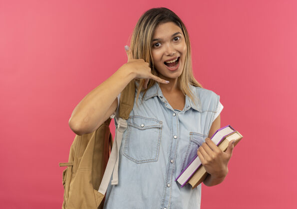 印象印象深刻的年轻漂亮的学生女孩穿着背包拿着书和做呼号孤立的粉红色抱穿粉色