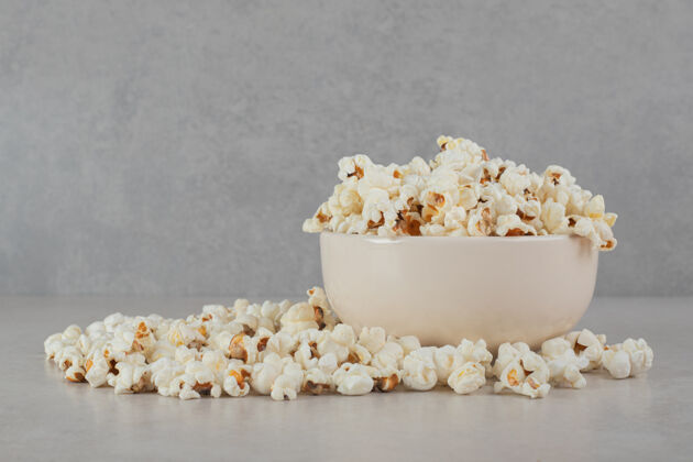 碗酥脆的爆米花在大理石表面的白色碗里和周围垃圾食品爆米花电影院