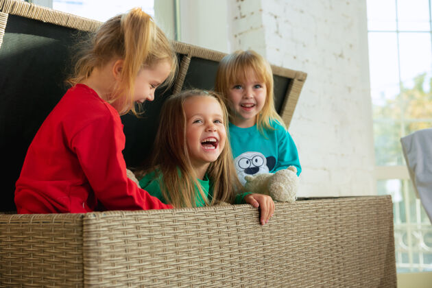 孩子穿着柔软保暖睡衣的小女孩在家里玩耍穿着五颜六色衣服的高加索儿童在一起玩得很开心童年 家里的舒适 幸福坐在一个大柳条盒子里笑着有趣地毯女孩
