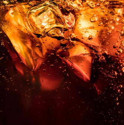 封闭深色可乐背景下冰块的特写镜头玻璃壁上有泡沫和大气泡的清凉甜味夏季饮料的质地起泡或漂浮到表面顶部冷立方体细节