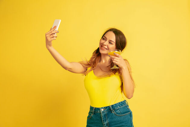 公司自拍 视频博客 微笑黄色工作室背景上的白人女性肖像美丽的女性模特人类情感的概念 面部表情 销售 广告夏季 旅游 度假手年轻表达