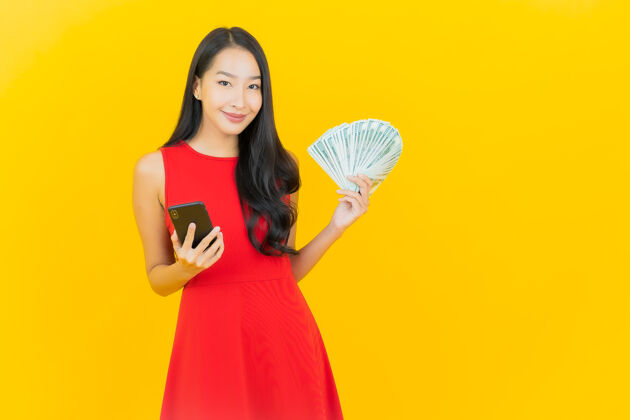 收入画像美丽的亚洲年轻女子微笑着在黄色的墙上有很多现金和金钱金钱账单金融