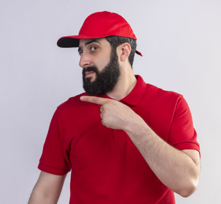 壁板年轻英俊的白人送货员穿着红色制服 戴着帽子 指着隔离在白色背景上的一侧帽子不愉快指向