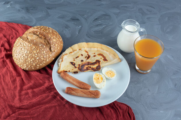 鸡蛋一盘煎饼 香肠和煮蛋片 旁边放着牛奶 果汁和面包 放在大理石表面上可口盘子美味