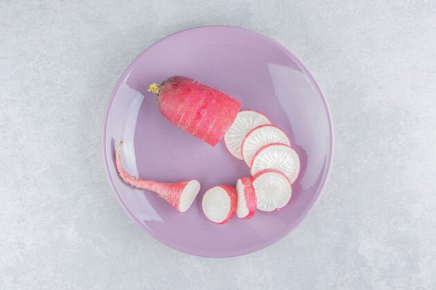 乡村成熟的萝卜片放在粉红色的盘子里 放在蓝色的表面上美味健康蔬菜