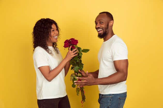 女性花为微笑情人节庆祝 快乐的非洲裔美国夫妇隔离在黄色工作室背景人类情感的概念 面部表情 爱 关系 浪漫的节日亲吻庆祝温柔