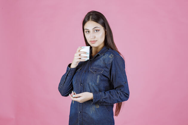 茶穿着牛仔衬衫的女孩正在享受一杯一次性咖啡人巧克力温暖