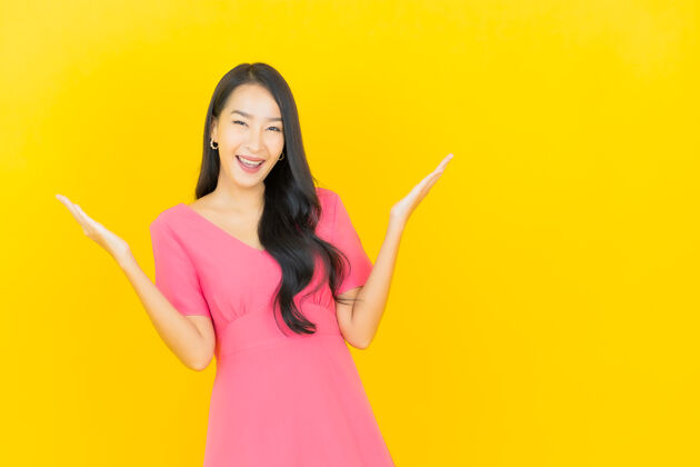 充满活力黄色墙壁上 美丽的亚洲年轻女子身着粉色连衣裙微笑的画像人中国人乐趣