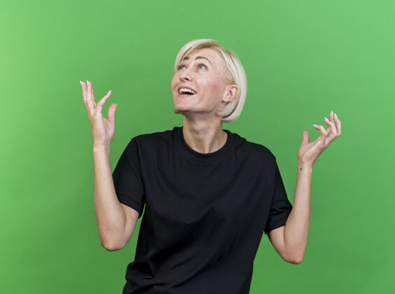 脸令人印象深刻的中年金发斯拉夫女人手举在空中看着隔离在绿色墙上印象斯拉夫人