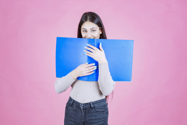 姿势女孩拿着一个蓝色的项目文件夹 把她的脸藏在后面女人人清单