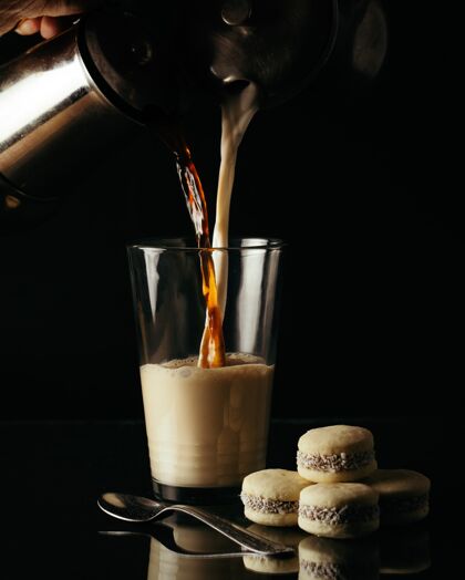 有机垂直拍摄的人倒茶和牛奶在一个玻璃杯在桌子上的饼干刷新背景液体