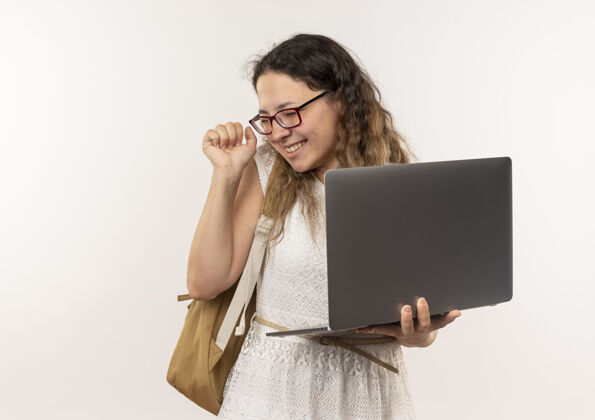 关闭快乐的年轻漂亮的女学生戴着眼镜 背着书包 拿着笔记本电脑 紧握拳头 闭着眼睛穿年轻举行