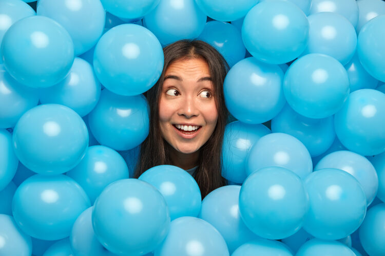 微笑快乐的少数民族妇女神秘地把目光投向一边 微笑着对着蓝色的气球 等待着特殊的活动有趣生日高兴