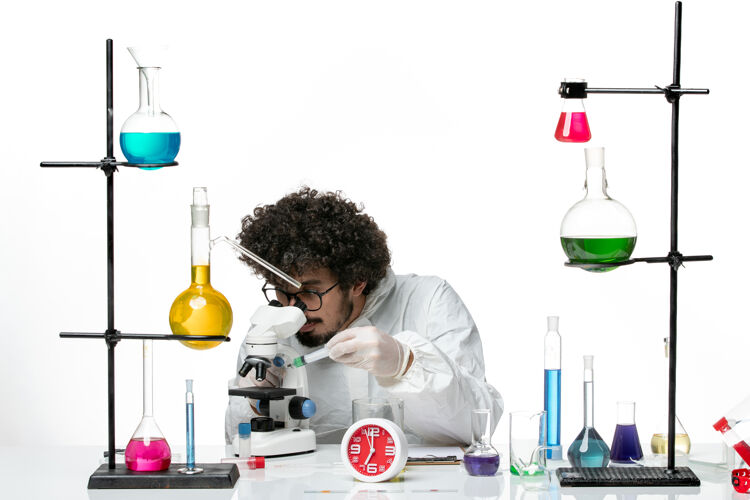烧杯前视图穿着特殊套装的年轻男科学家在白墙上使用显微镜科学特殊套装