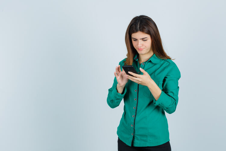 水平穿着绿衬衫的年轻女士在手机上打字 看上去很忙 正对着前方看早晨人员计算机