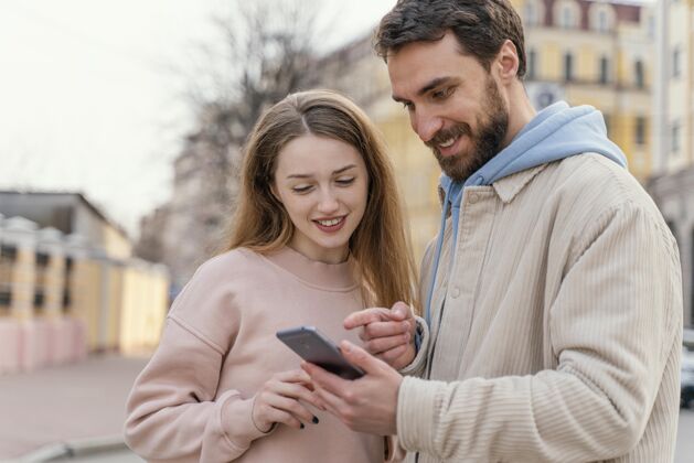 微笑笑脸夫妇在城市户外使用智能手机的前视图情侣城市户外乐趣