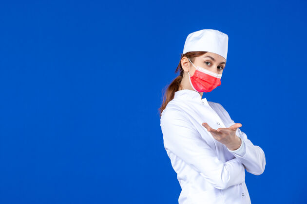 医学正面图蓝色墙上戴着红色面罩的年轻护士 穿着医疗服人年轻护士套装