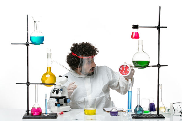 化学正面图身穿特殊套装的年轻男性科学家戴着防护头盔 在白墙上拿着时钟科学实验室科维德-化学男科学玻璃特殊