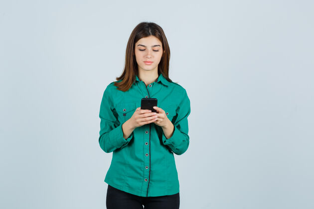 工作穿着绿色上衣 黑色裤子 神情专注的年轻女孩在手机上写信息正视图课堂课裤子大学