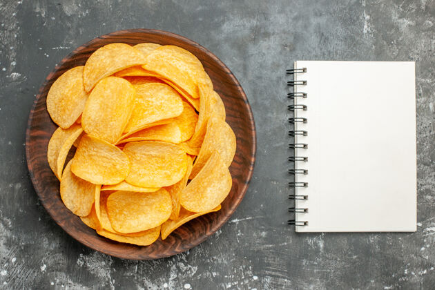 薯片美味的自制薯片放在棕色的盘子里 笔记本放在灰色的桌子上零食新鲜薯片