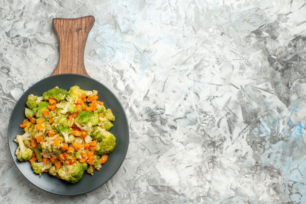 胡椒新鲜健康的蔬菜沙拉放在白色桌子左侧的木制砧板上新鲜饮食菜肴