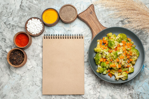 美食健康蔬菜沙拉不同香料的水平视图和白色桌子上的笔记本蔬菜米饭午餐