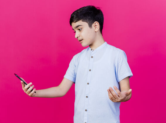 不知所措不知所措的年轻白人男孩拿着手机 看着手机 在深红的背景下显示出孤立的空手秀着抱着男孩