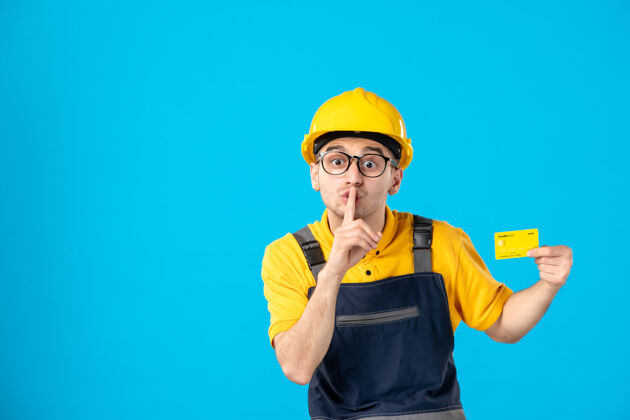 信用卡身穿制服 头戴钢盔 信用卡要求在蓝色墙上保持沉默的男性建筑工人正面图建筑工专业制服